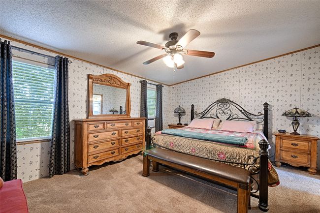 Bedroom featuring ornamental molding, a textured ceiling, wallpapered walls, a ceiling fan, and light colored carpet | Image 11