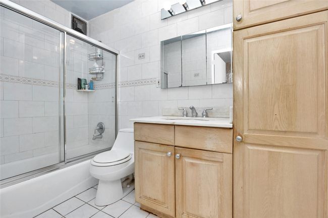 Full bath featuring vanity, tile patterned floors, tile walls, shower / bath combination with glass door, and backsplash | Image 9