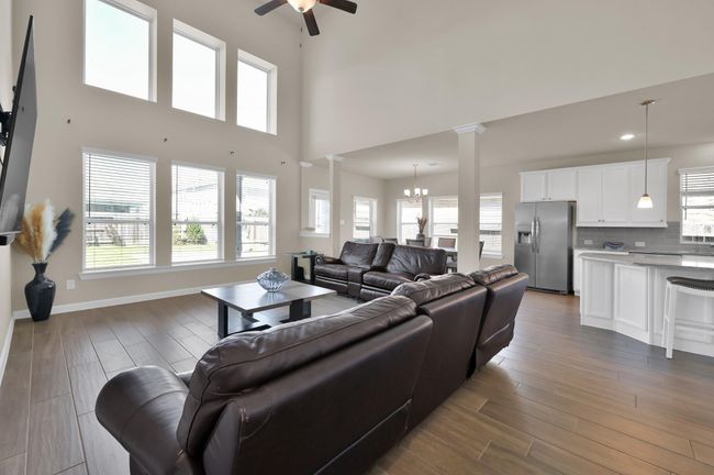 This open floor plan connects the Living Room, Dining, and Kitchen. Floor to ceiling windows provide impressive natural light and show off the dramatic ceiling height. | Image 12