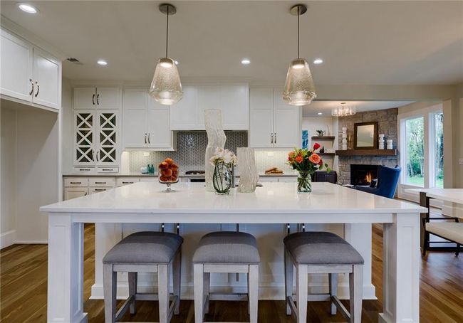 Kitchen featuring wood-type flooring, white cabinetry, decorative light fixtures, and a stone fireplace | Image 15