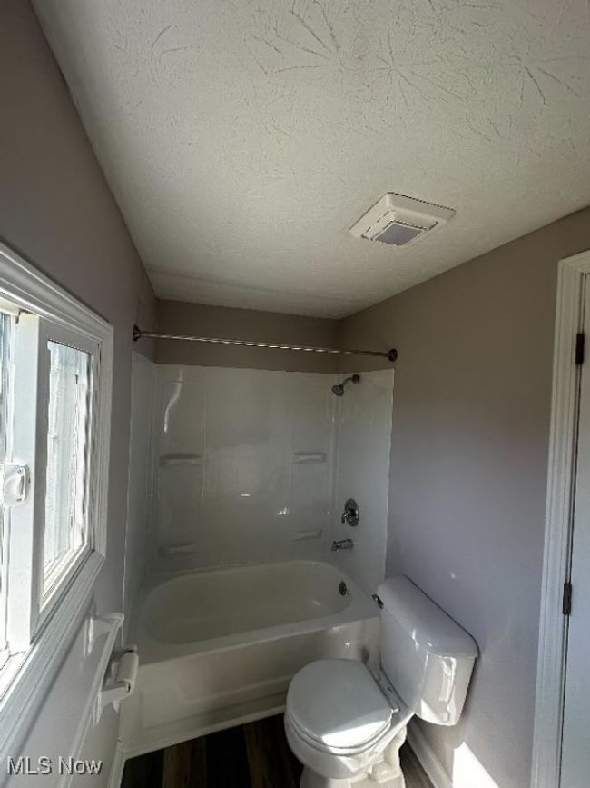 Bathroom featuring shower / bathing tub combination, hardwood / wood-style flooring, toilet, and a textured ceiling | Image 8