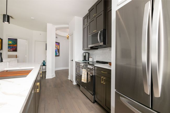 Kitchen with appliances with stainless steel finishes, decorative backsplash, dark wood-style flooring, and light stone counters | Image 13