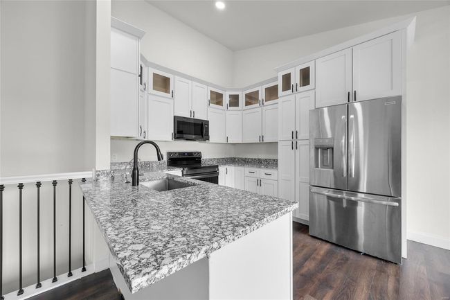 Kitchen featuring a peninsula, stainless steel refrigerator with ice dispenser, white cabinetry, black range with electric stovetop, and a sink | Image 26