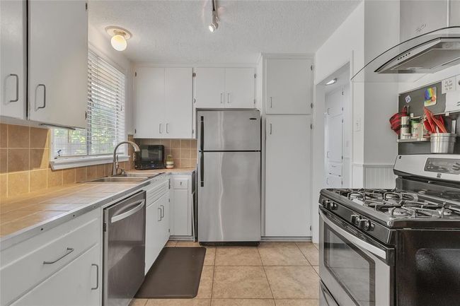 Kitchen with stainless steel appliances, wall chimney exhaust hood, tile counters, white cabinetry, and a textured ceiling | Image 7