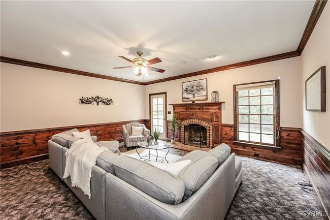 Carpeted living area with a wainscoted wall, healthy amount of natural light, ceiling fan, wood walls, and a fireplace | Image 13