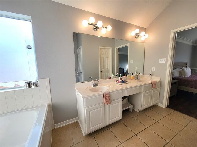 A bright, spacious bathroom with dual sinks, a large mirror, modern lighting, and a soaking tub. It connects to a bedroom, offering convenience and style. | Image 21