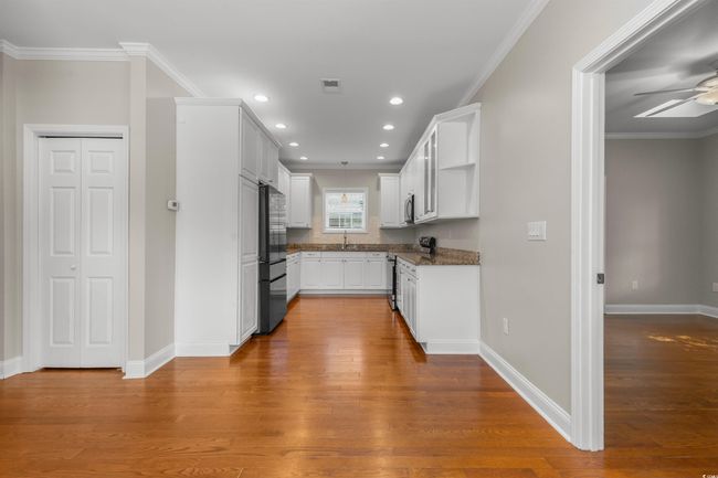 Kitchen with freestanding refrigerator, stainless steel range with electric stovetop, wood finished floors, white cabinets, and crown molding | Image 11