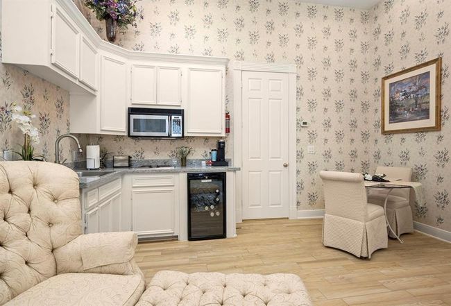This cozy kitchen area located in the sitting area of this suite features cream cabinetry, granite countertops, and modern appliances, complemented by floral wallpaper and hardwood flooring. A small dining nook adds charm, perfect for intimate meals. | Image 17