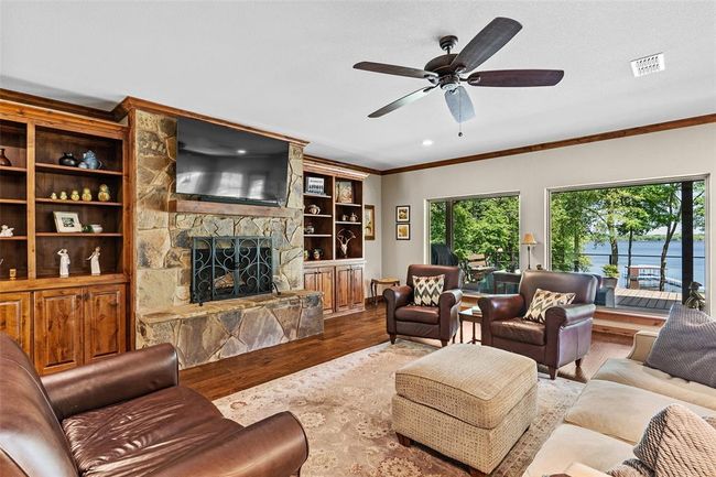 Living room with a stone fireplace, a water view, ceiling fan, wood-type flooring, and ornamental molding | Image 5