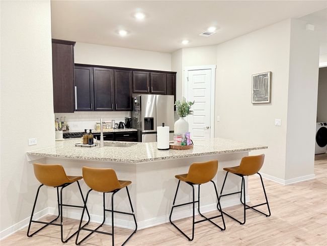 Kitchen with light stone countertops, washer / clothes dryer, stainless steel refrigerator with ice dispenser, and a breakfast bar | Image 9