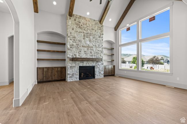 Unfurnished living room with beamed ceiling, high vaulted ceiling, light wood finished floors, arched walkways, and a stone fireplace | Image 11