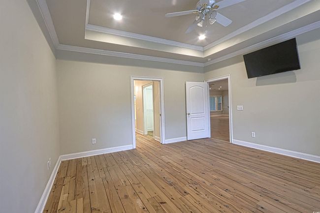 Unfurnished bedroom featuring ornamental molding, wood-type flooring, a tray ceiling, recessed lighting, and a ceiling fan | Image 11