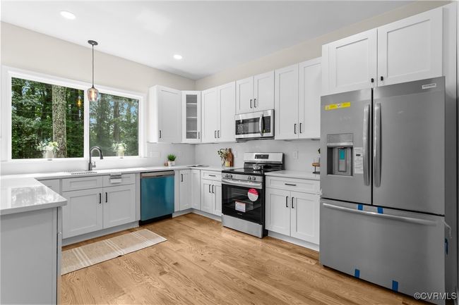 Kitchen featuring stainless steel appliances, light wood finished floors, white cabinetry, decorative light fixtures, and light countertops | Image 11