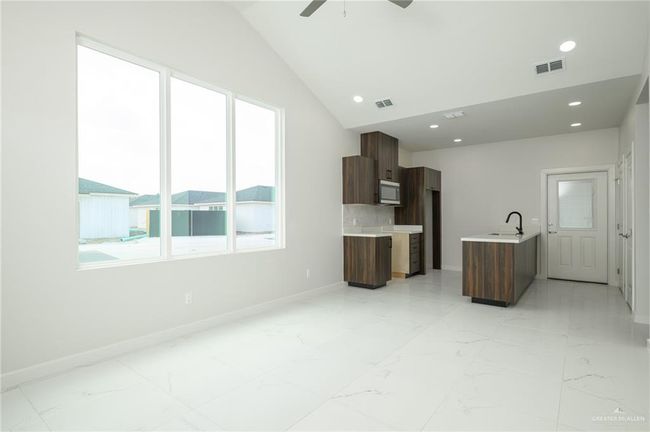 Unfurnished living room featuring plenty of natural light, a sink, light marble finish floors, lofted ceiling, and recessed lighting | Image 6