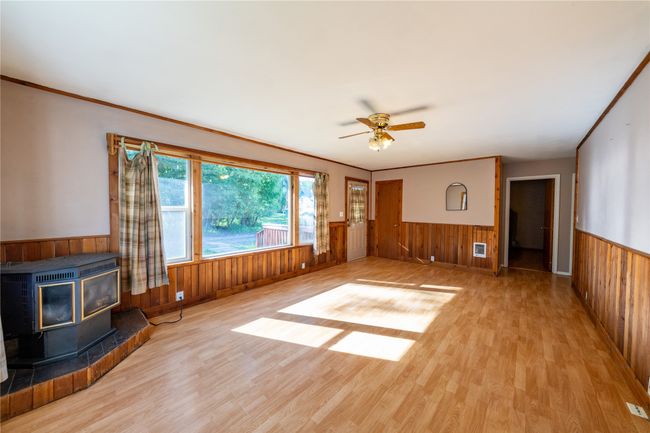 Unfurnished living room featuring a wainscoted wall, wood walls, wood finished floors, a wood stove, and a ceiling fan | Image 6