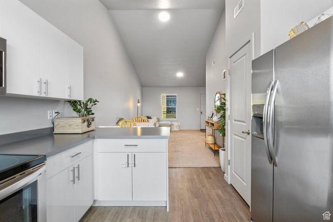 Kitchen with visible vents, a peninsula, white cabinetry, light wood-style floors, and stainless steel fridge with ice dispenser | Image 15