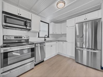 Kitchen with white cabinets, light wood-type flooring, light stone countertops, stainless steel appliances, and sink | Image 2