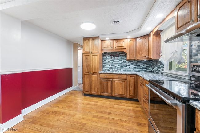 Kitchen featuring stainless steel electric stove, brown cabinets, light wood-style flooring, and a sink | Image 15