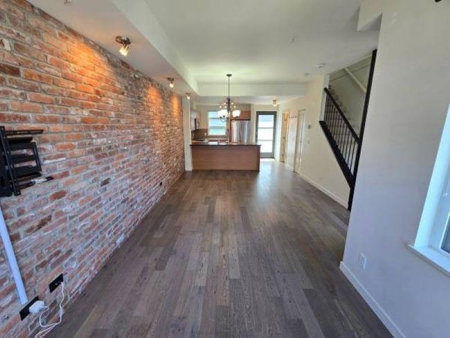 Hallway with dark wood finished floors, a chandelier, baseboards, brick wall, and stairway | Image 5