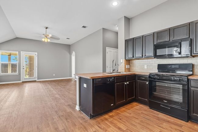 Kitchen featuring a peninsula, black appliances, open floor plan, decorative backsplash, and arched walkways | Image 10