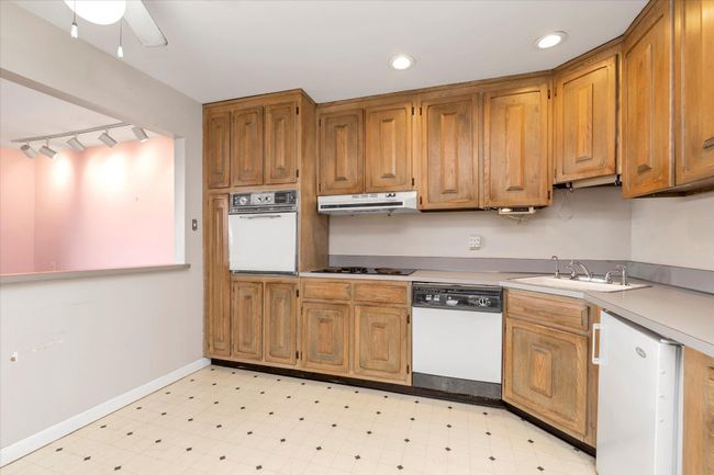 Kitchen with under cabinet range hood, white appliances, light countertops, light floors, and brown cabinetry | Image 14