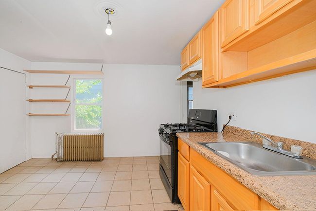 Kitchen featuring gas stove, under cabinet range hood, radiator, light countertops, and light tile patterned floors | Image 10