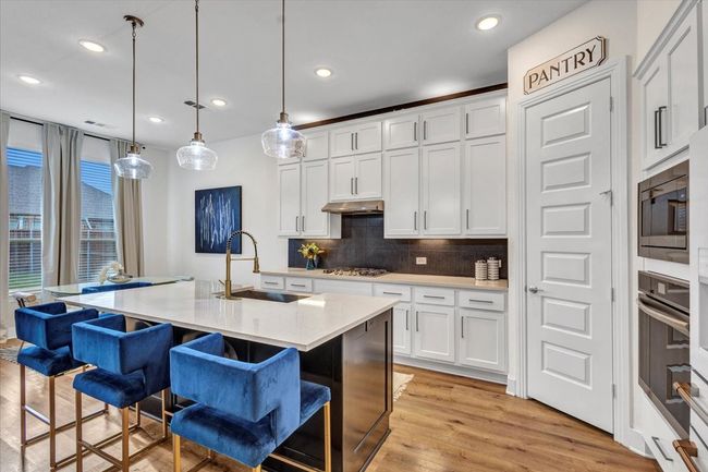 Kitchen featuring stainless steel appliances, farm sink, a breakfast bar area, decorative backsplash, and white cabinetry | Image 16