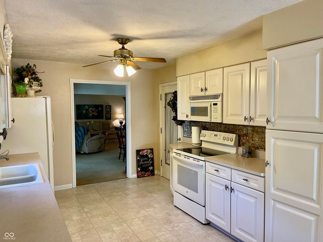 kitchen featuring white appliances, ceiling fan, light countertops, white cabinetry, and decorative backsplash | Image 27