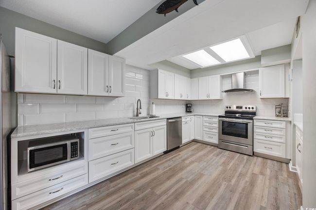 Kitchen with stainless steel appliances, wall chimney exhaust hood, a sink, light wood-type flooring, and backsplash | Image 12