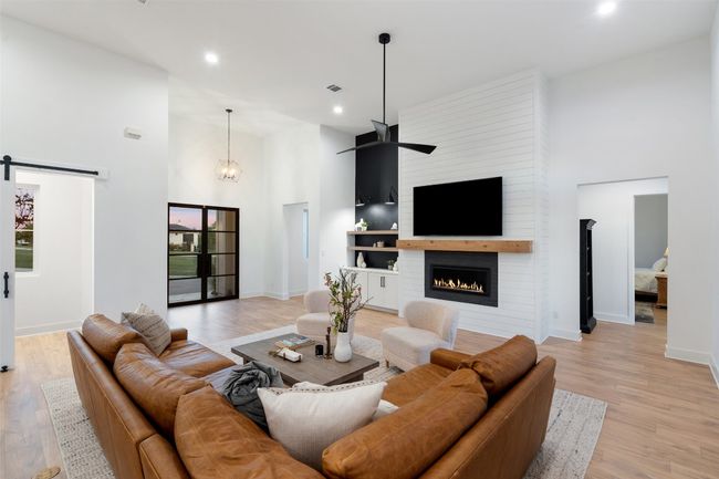 Living area featuring a high ceiling, a barn door, recessed lighting, light wood-type flooring, and a fireplace | Image 7