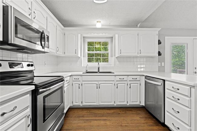 Kitchen with appliances with stainless steel finishes, dark wood-style flooring, a textured ceiling, white cabinets, and light countertops | Image 12