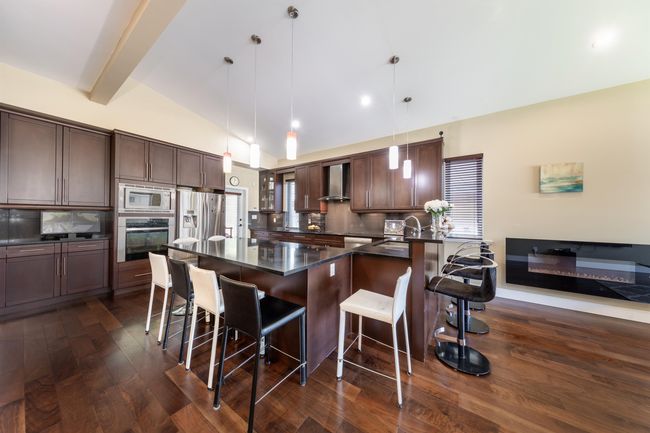 Kitchen with appliances with stainless steel finishes, dark countertops, wall chimney range hood, dark wood-style floors, and a kitchen breakfast bar | Image 13