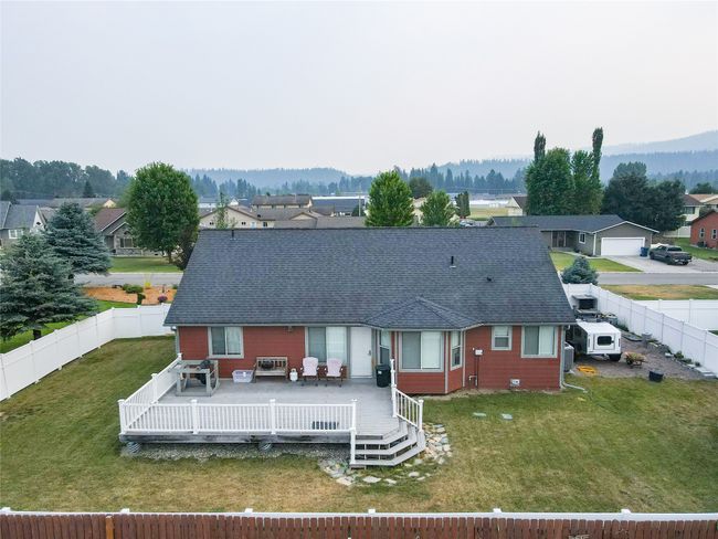 Rear view of house with a yard, a fenced backyard, a deck with mountain view, and roof with shingles | Image 23