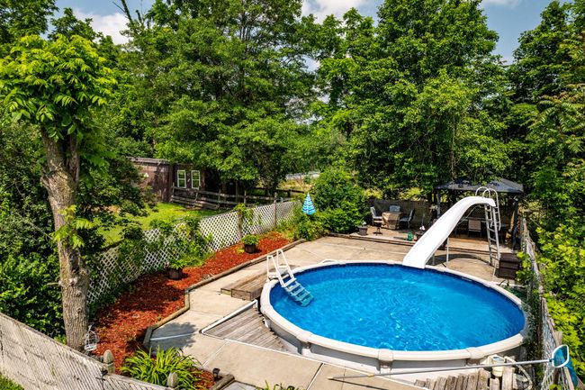 View of pool featuring a water slide, a fenced backyard, a patio, and view of wooded area | Image 37