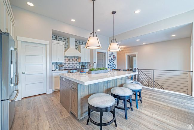 Kitchen featuring custom exhaust hood, high end refrigerator, light wood-style flooring, a breakfast bar, and recessed lighting | Image 11