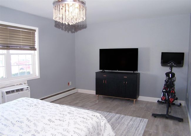 Bedroom with an inviting chandelier, hardwood / wood-style floors, a wall unit AC, and baseboard heating | Image 8
