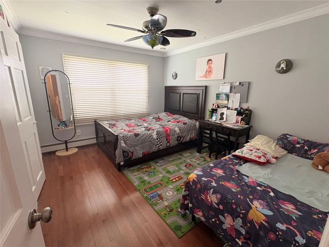 Bedroom with baseboard heating, hardwood / wood-style flooring, crown molding, and a ceiling fan | Image 8