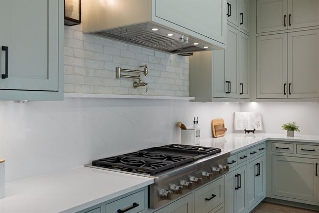 Kitchen featuring stainless steel gas cooktop, light countertops, wall chimney exhaust hood, and decorative backsplash | Image 16