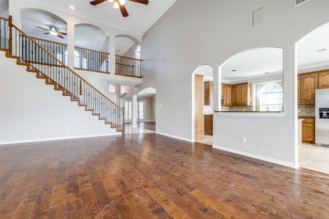Unfurnished living room with stairway, a ceiling fan, wood finished floors, baseboards, and a high ceiling | Image 6