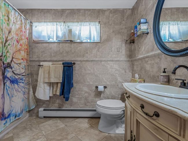 Full bath featuring baseboard heating, vanity, curtained shower, tile walls, and tile patterned flooring | Image 24