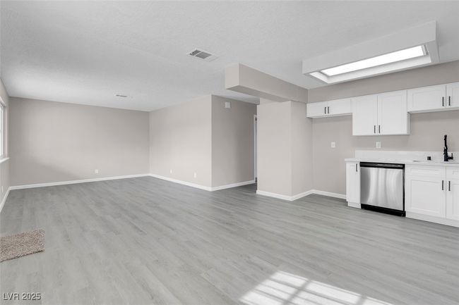 Unfurnished living room with a textured ceiling, a sink, light wood-style flooring, baseboards, and visible vents | Image 6