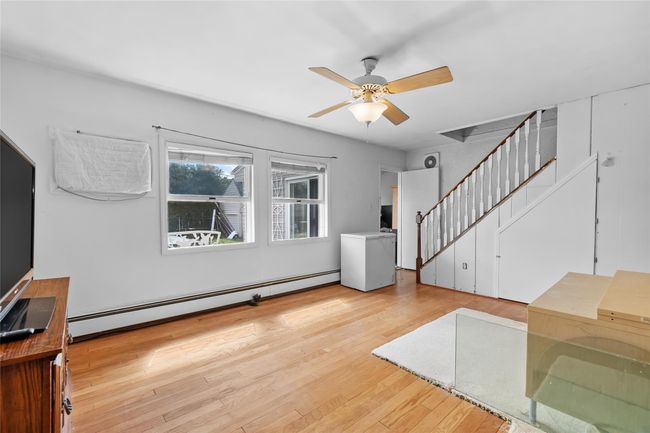 Living room with a baseboard radiator, wood finished floors, stairway, and a ceiling fan | Image 10