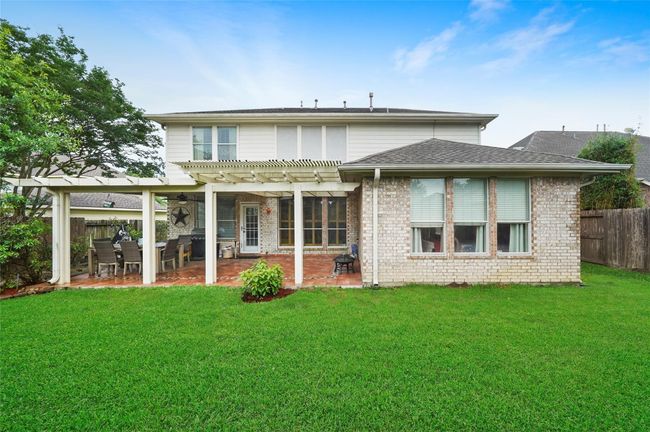 The backyard offers a spacious covered patio featuring a pergola. The exterior is brick with large windows, and the yard is well-maintained with lush green grass, providing a great space for outdoor activities and relaxation. | Image 28