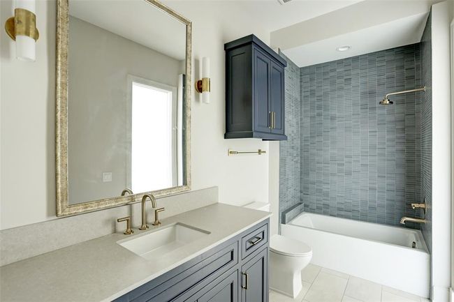 This stylish en-suite bath boasts a refined shower/tub combo adorned with mosaic stone tile, a sleek modern vanity with a rich wooden countertop, and an elegant framed mirror, blending sophistication with functionality. | Image 21
