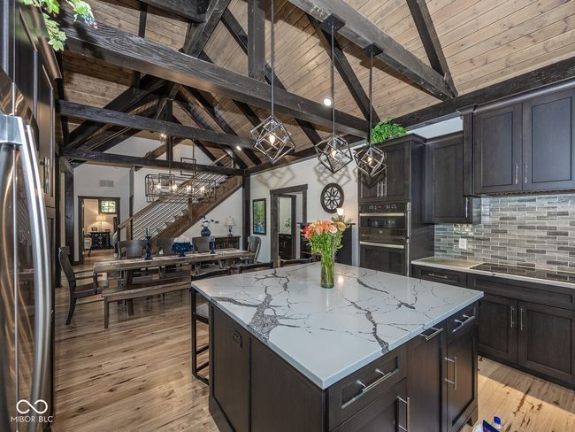 kitchen with appliances with stainless steel finishes, a chandelier, tasteful backsplash, a center island, and light stone countertops | Image 17