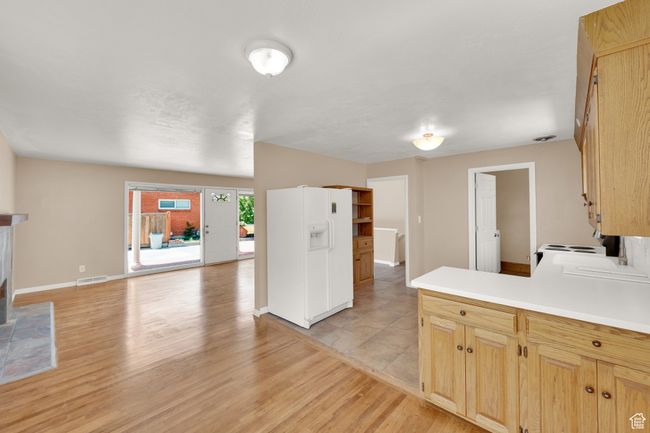Kitchen with light wood-type flooring, light countertops, white fridge with ice dispenser, baseboards, and a peninsula | Image 4