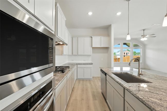 Kitchen featuring stainless steel appliances, light wood finished floors, white cabinetry, decorative light fixtures, and light stone countertops | Image 5