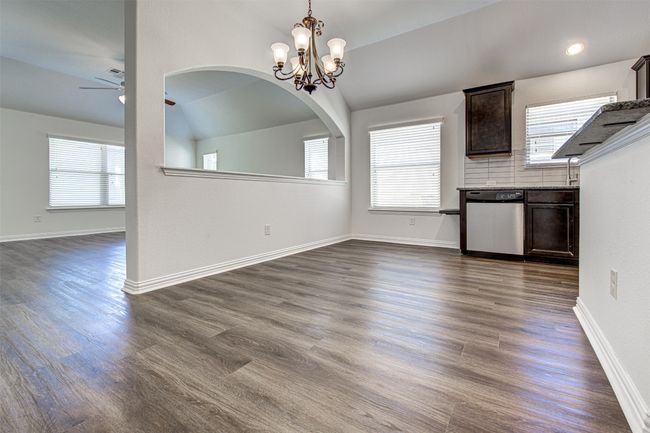 Unfurnished dining area featuring ceiling fan, dark wood-style floors, a chandelier, vaulted ceiling, and arched walkways | Image 23
