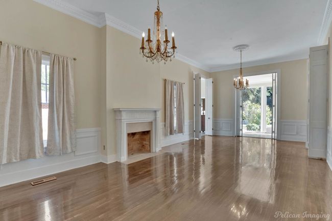 Unfurnished living room with a chandelier, a wainscoted wall, wood finished floors, a decorative wall, and ornamental molding | Image 11