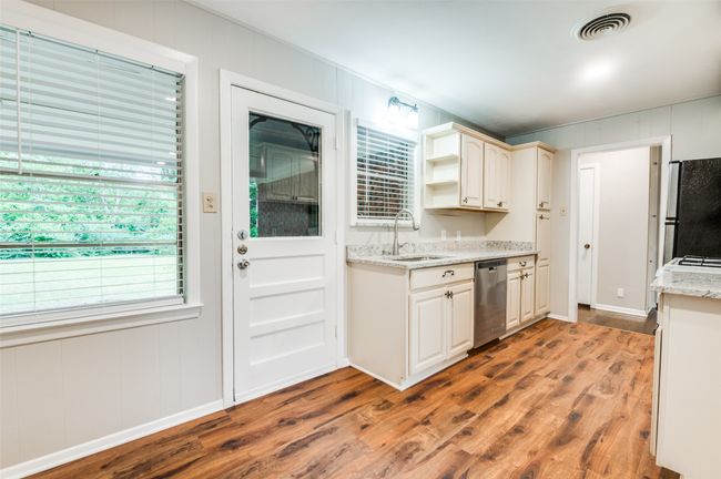 Kitchen with appliances, a sink, wood look finished floors, shelves, and a dining area. | Image 10